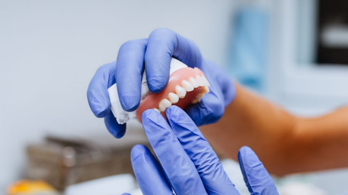 Dentiste tenant un ensemble de prothèses dentaires avec des mains gantées.