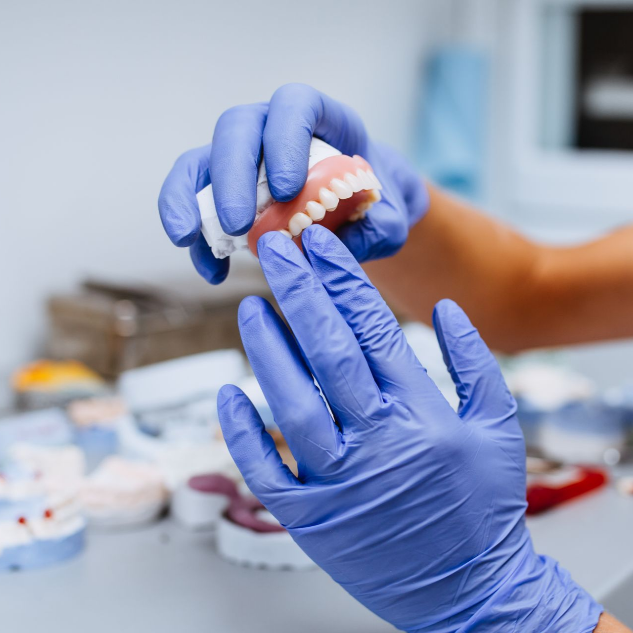 Mains dans des gants bleus tenant un ensemble de prothèses dentaires dans un laboratoire dentaire.