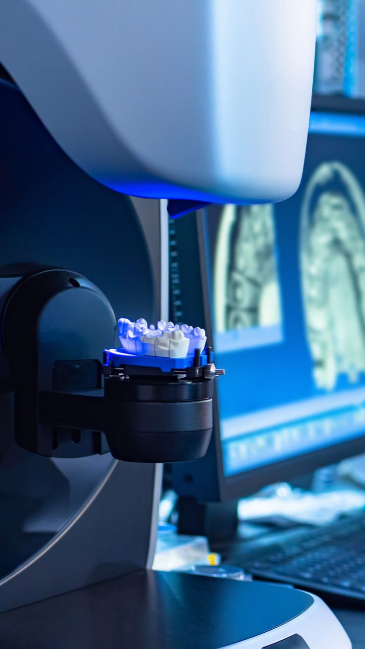 Modèle dentaire scanné par une machine éclairée en bleu, écran d'ordinateur avec scans dentaires en arrière-plan.