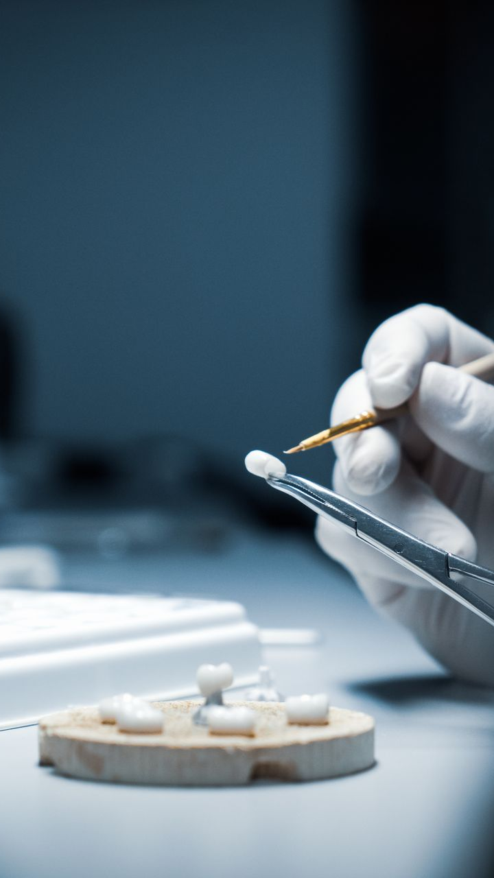 Une main gantée tient des outils dentaires pour examiner une couronne dentaire blanche dans un laboratoire.