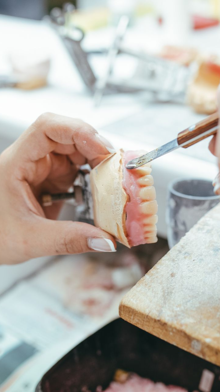 Personne travaillant sur une prothèse dentaire, utilisant un petit outil pour façonner un matériau rose attaché à un moule.