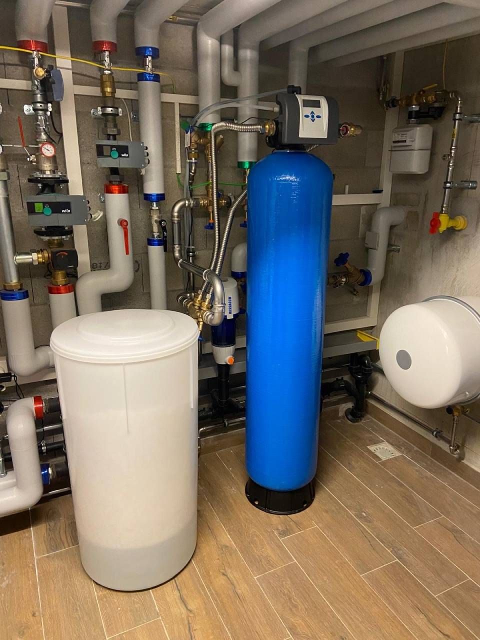 Un filtre à eau bleu est placé à côté d'un réservoir blanc dans une pièce remplie de tuyaux.