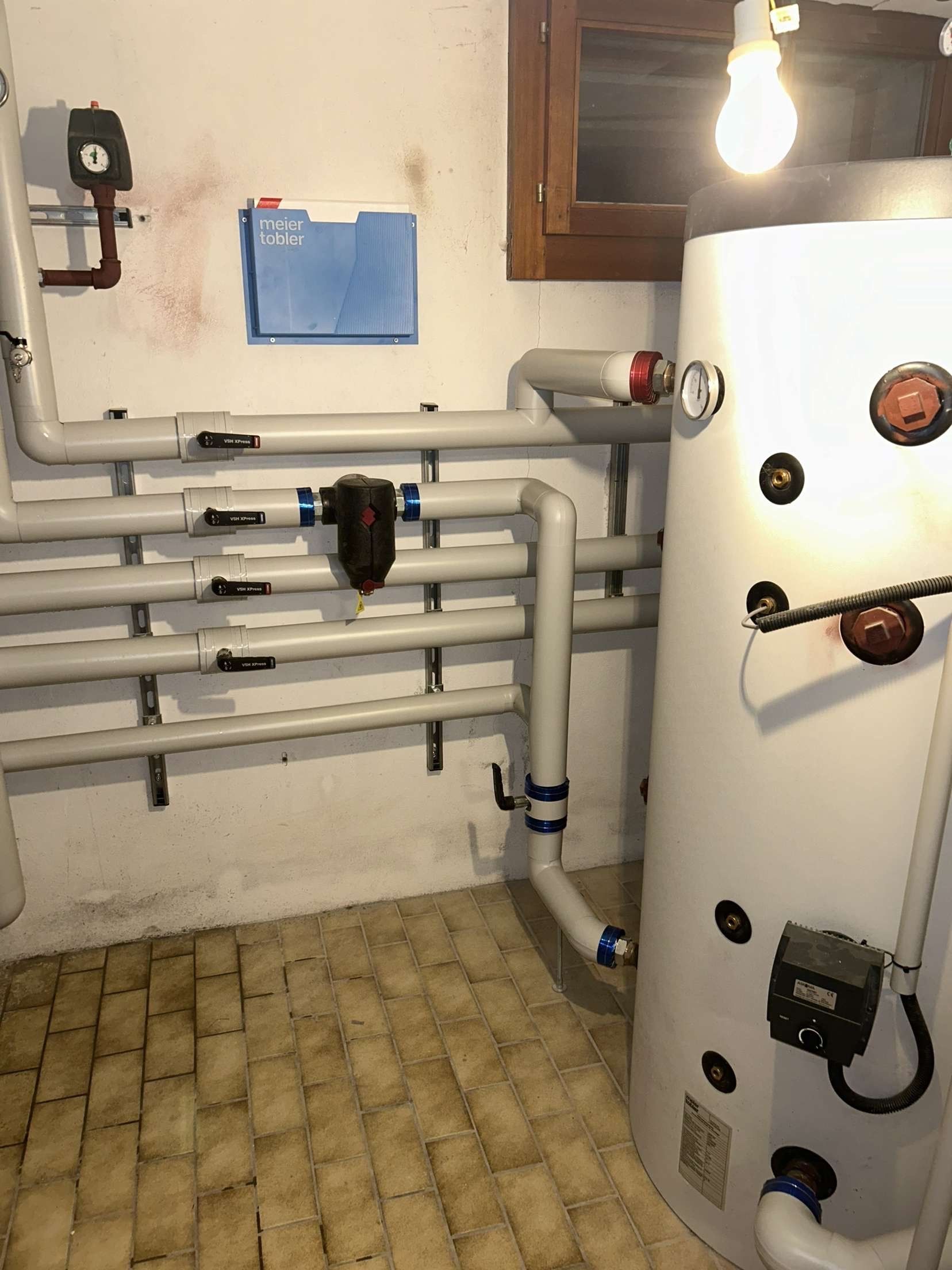 Une pièce avec un chauffe-eau et des tuyaux sur le mur.