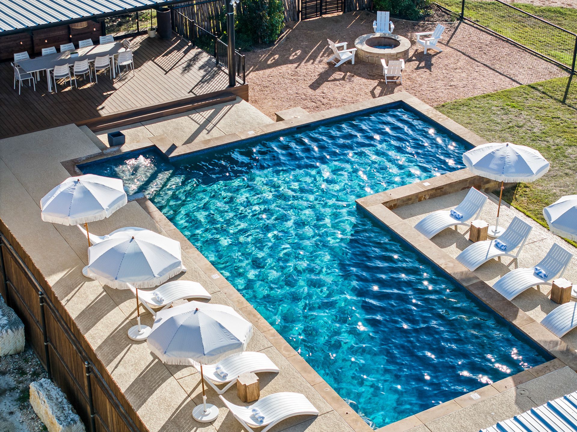 Outdoor pool with lounge chairs, umbrellas, and a fire pit; dining area in background.