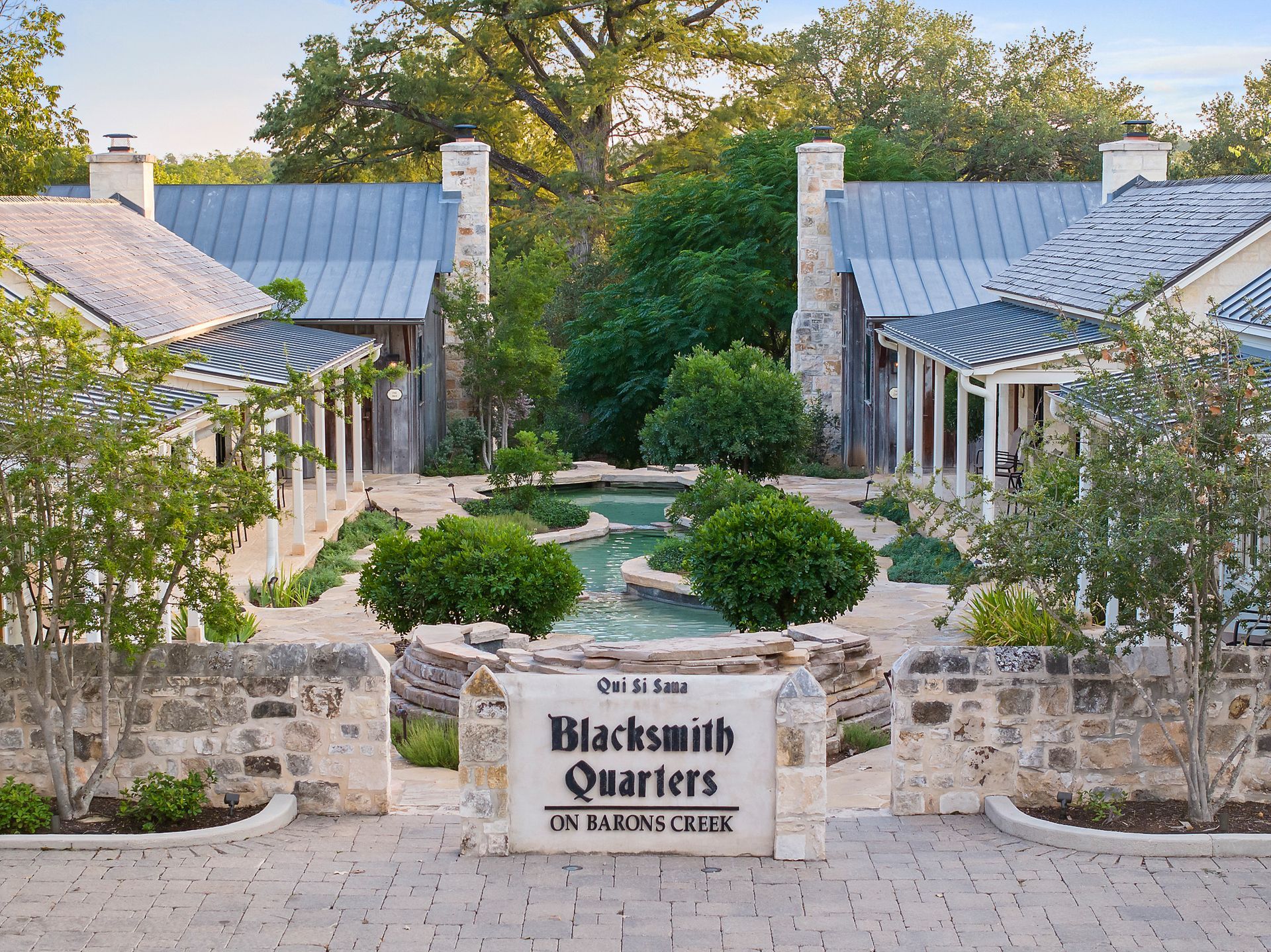 Blacksmith Quarters sign in front of stone buildings with a water feature, trees and greenery.