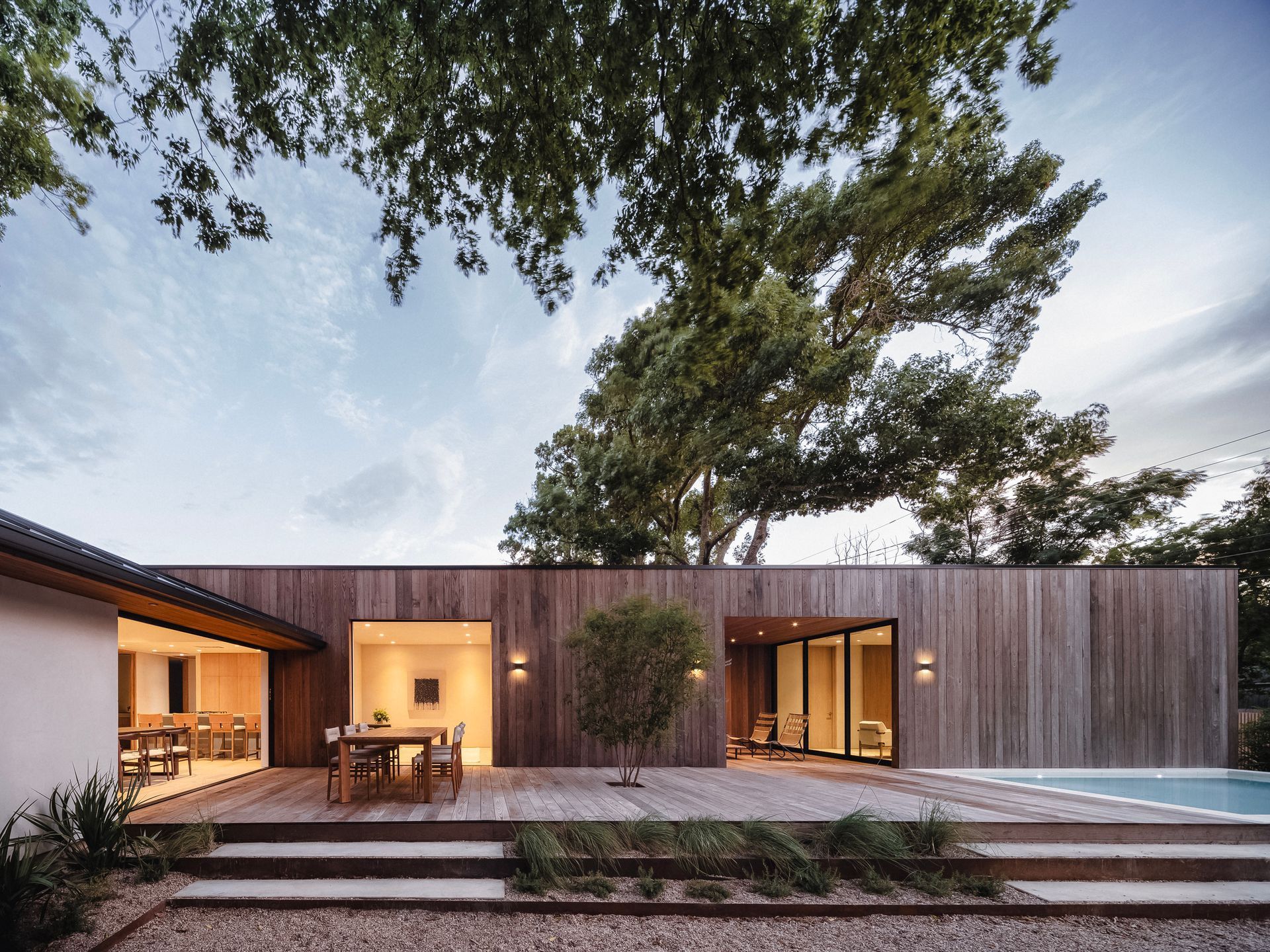 Modern wooden house with deck and pool, under a tree.