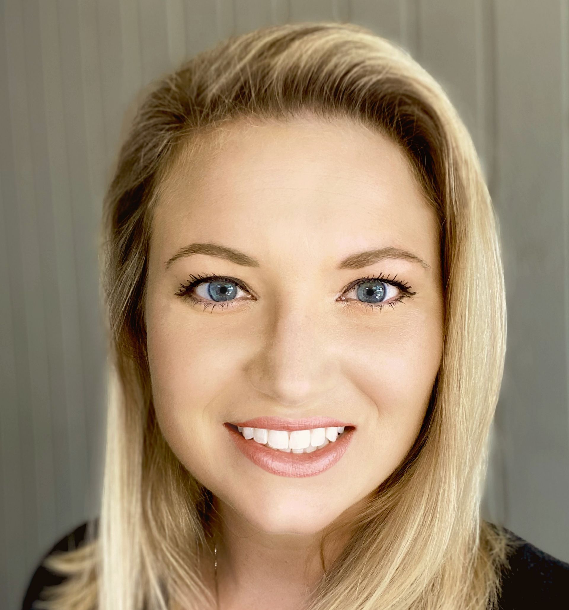 Blond woman with blue eyes smiling, looking at the camera.