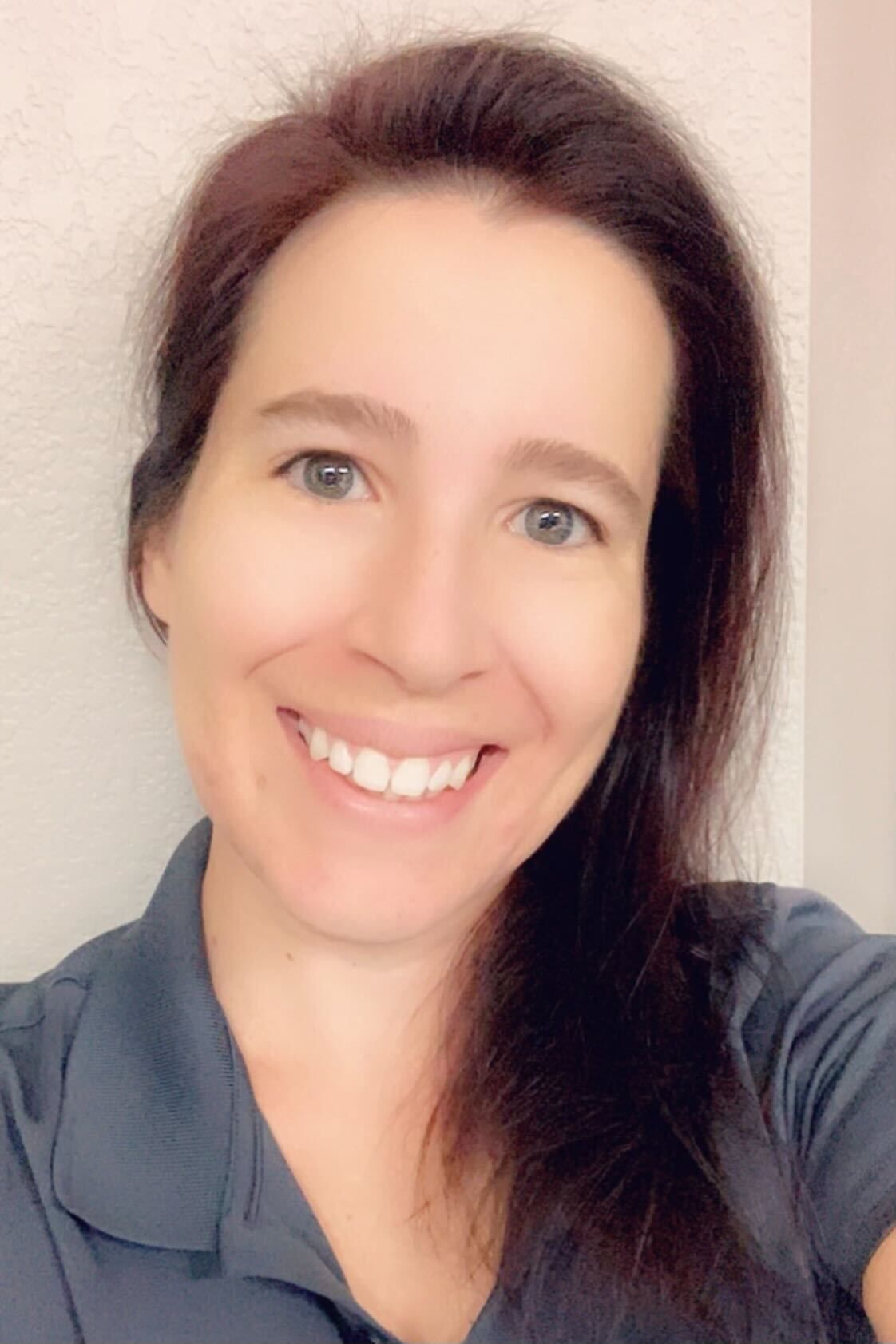 Woman with red-brown hair, smiling, wearing a blue shirt, against a plain background.