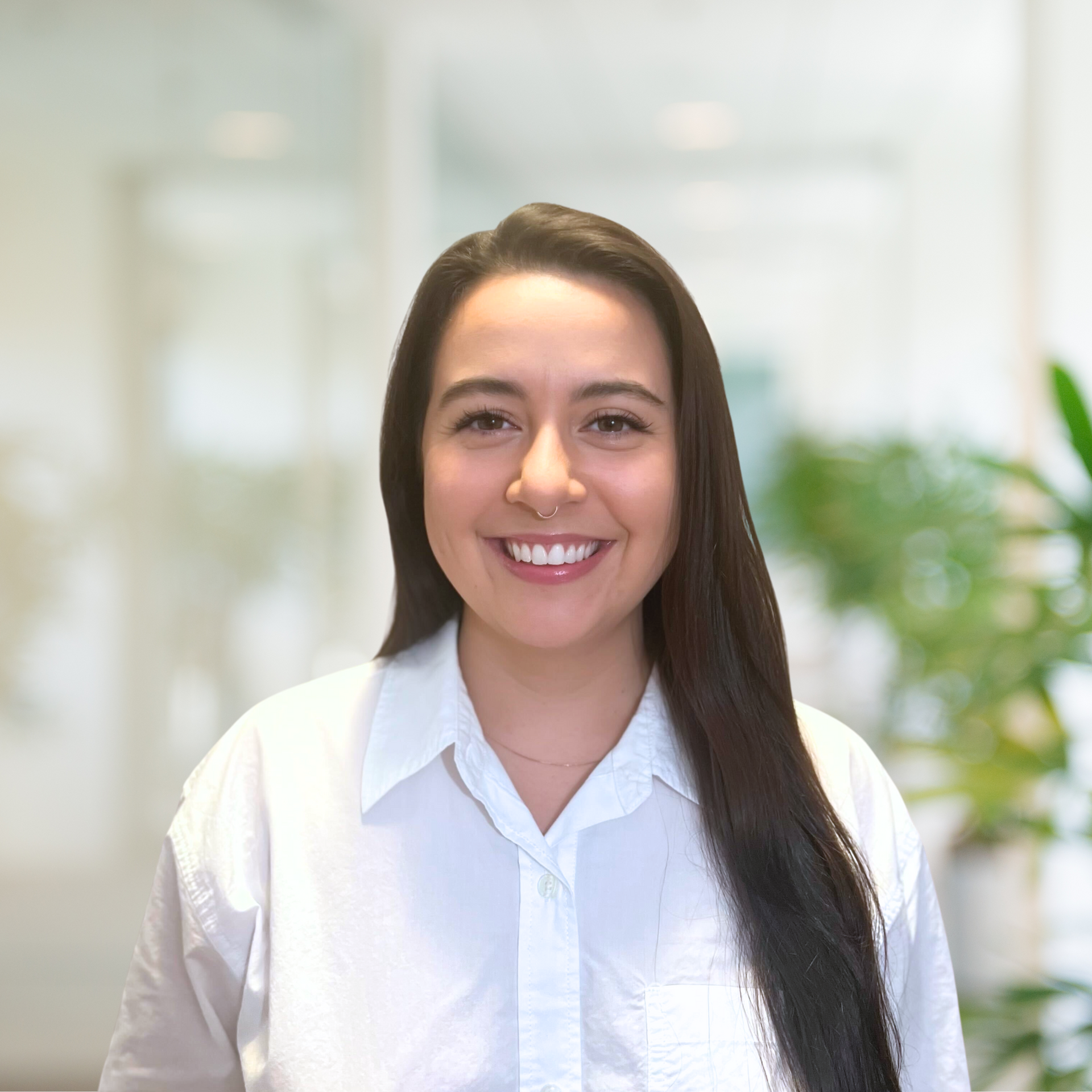 Woman with long dark hair and a nose ring smiling in a white button-down shirt.