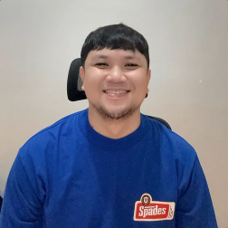 Smiling man in blue shirt with a Spades logo, seated indoors, facing the camera.