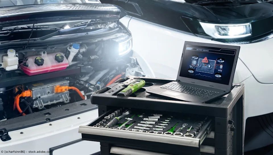 Motorraum mit Diagnosegeräten und Laptop auf einem Wagen, helle Arbeitsleuchten in einer Garage