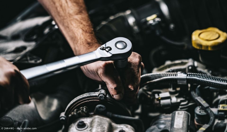 Ein Mechaniker benutzt einen Ratschenschlüssel, um in einer Garage an einem Automotor zu arbeiten.