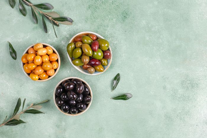 Tres cuencos de diferentes tipos de aceitunas sobre una mesa verde.