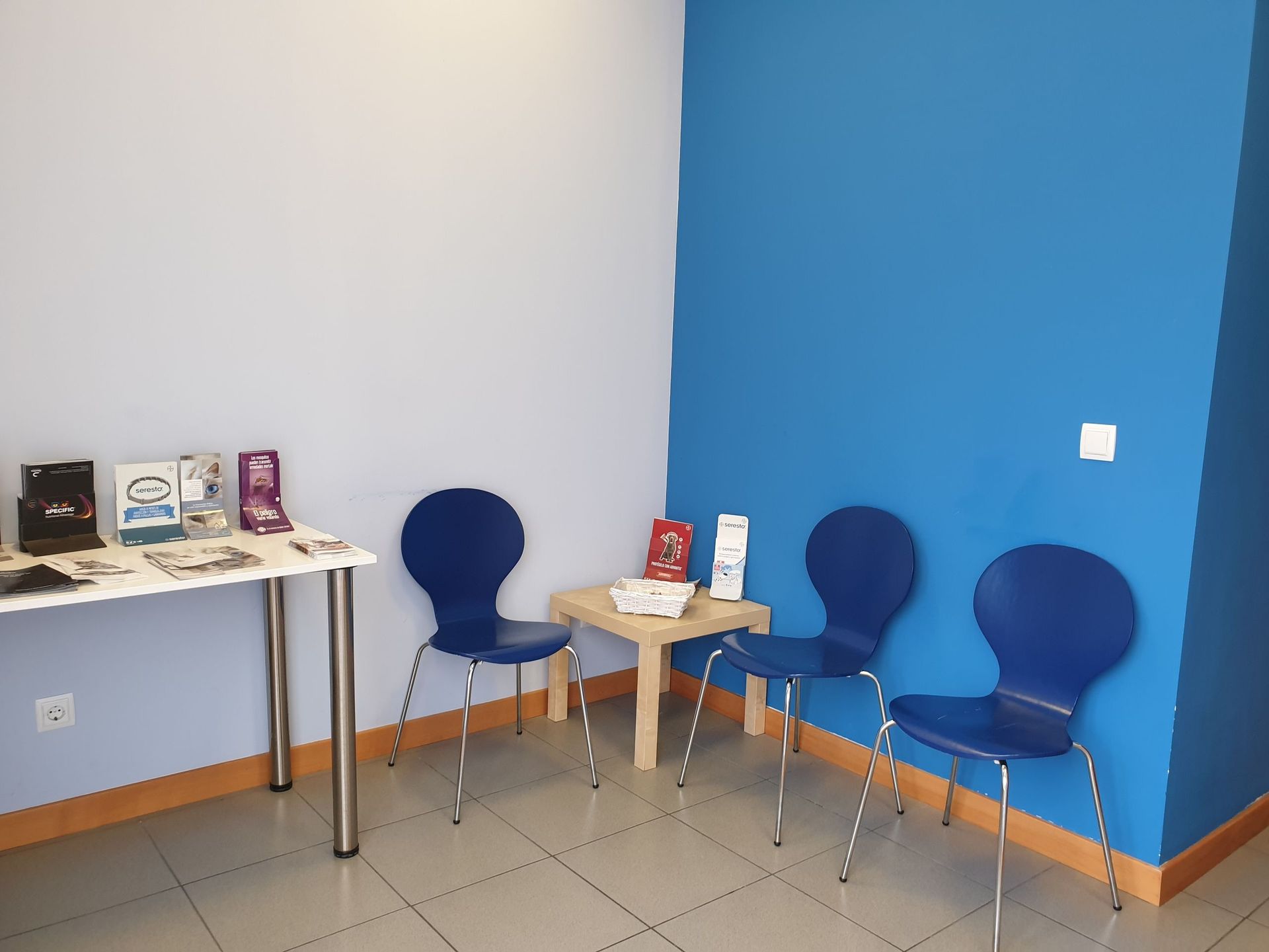 Una sala de espera con sillas azules y una mesa.