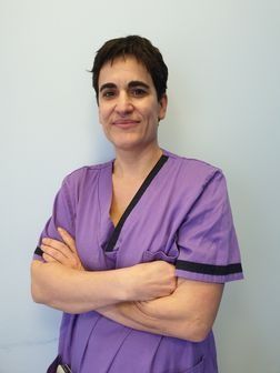 Una mujer con un uniforme morado está de pie con los brazos cruzados.