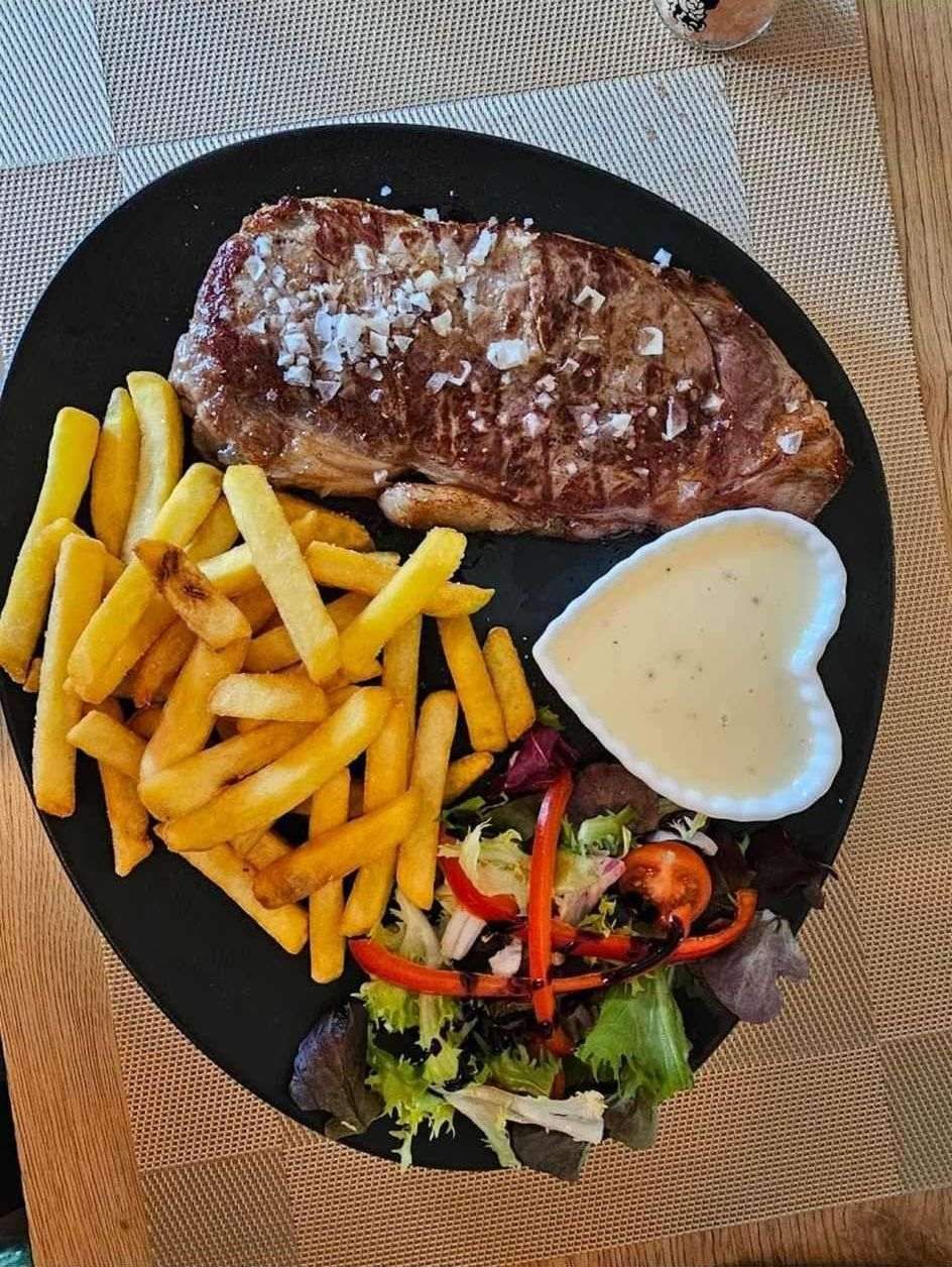 Cena de bistec en plato negro: bistec a la parrilla con sal marina, papas fritas, ensalada.