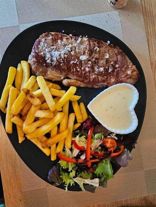 Cena de bistec en plato negro: bistec a la parrilla con sal marina, papas fritas y ensalada.