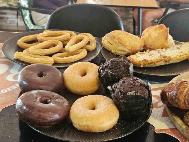 Una mesa de productos horneados, incluyendo donas, magdalenas, croissants y aros de cebolla.