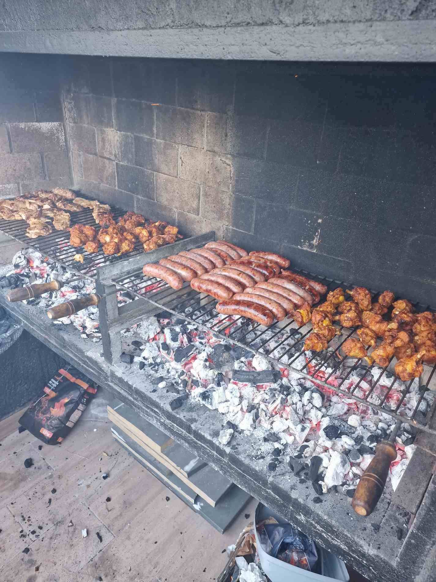 Barbacoa con salchichas, pollo y parrilladas de carbón en un entorno de chimenea de piedra.