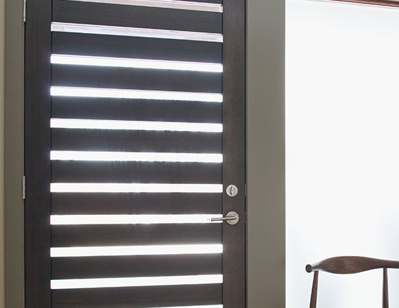 Porte en bois foncé avec fentes horizontales, poignée argentée et un mur blanc à côté.