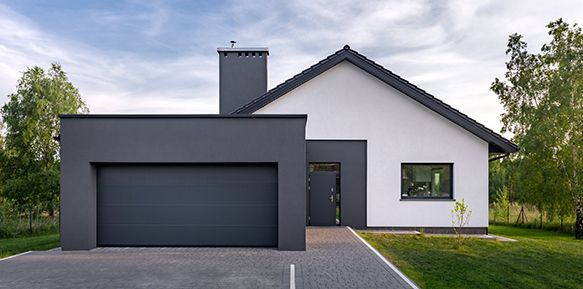 Maison moderne avec garage gris, cheminée et façade blanche. Allée en briques, pelouse verte et arbres.