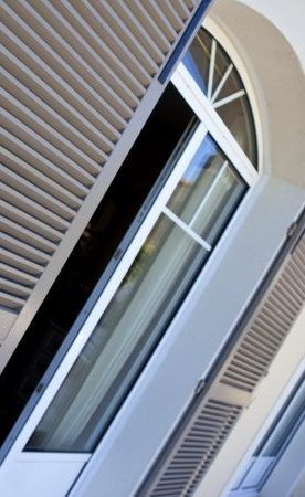 Fenêtre cintrée blanche avec volets ouverts à lamelles.
