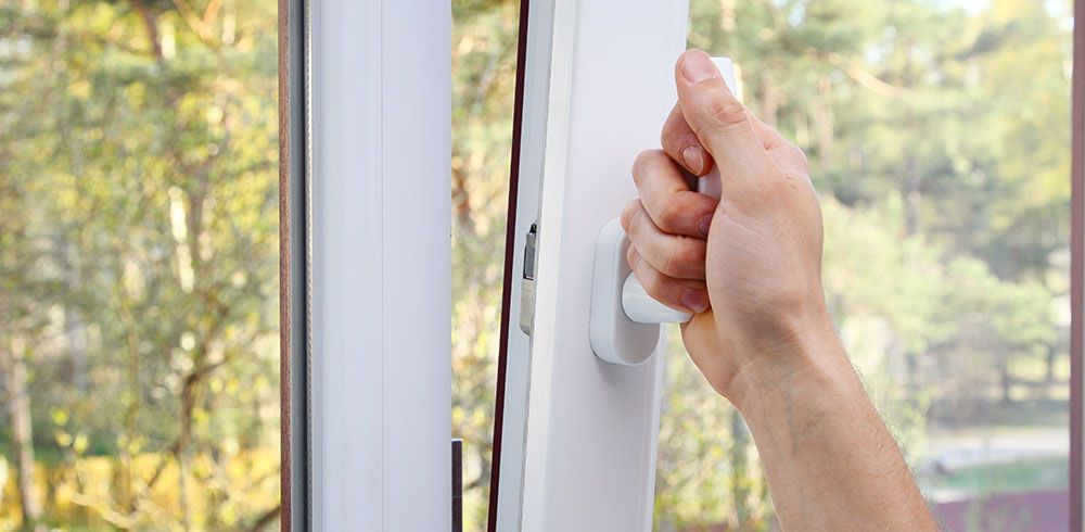 La main d'une personne ouvrant une fenêtre blanche, avec une vue sur les arbres par la fenêtre.