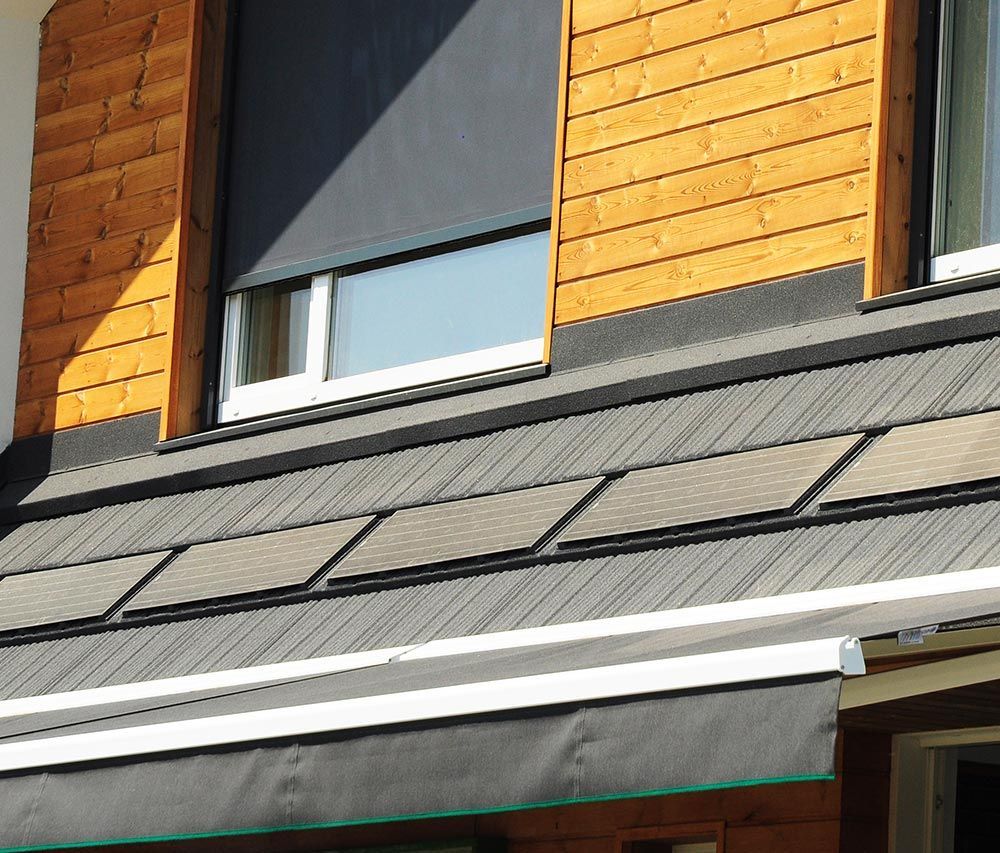 Vue extérieure d'un bâtiment avec des panneaux solaires sur le toit et une fenêtre avec un auvent rétractable.