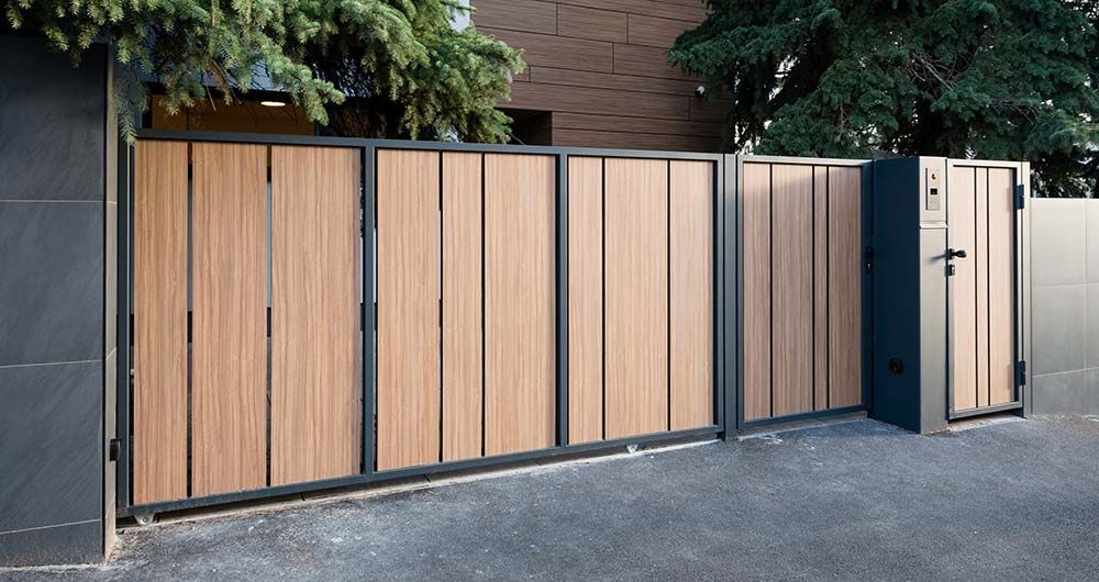 Portail en bois à panneaux verticaux dans un cadre en métal noir, ouvrant sur une allée.