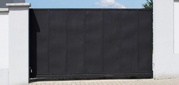 Portail coulissant noir entre deux piliers blancs.