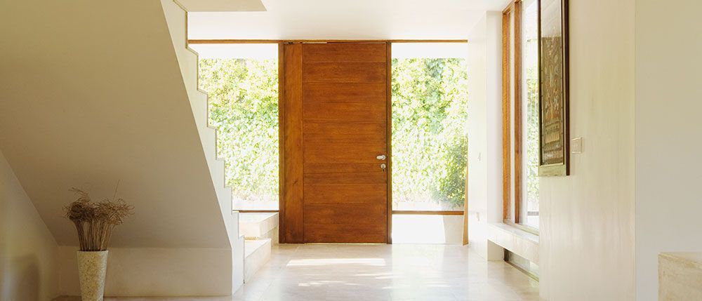 Entrée avec porte en bois, escalier et lumière naturelle éclatante.