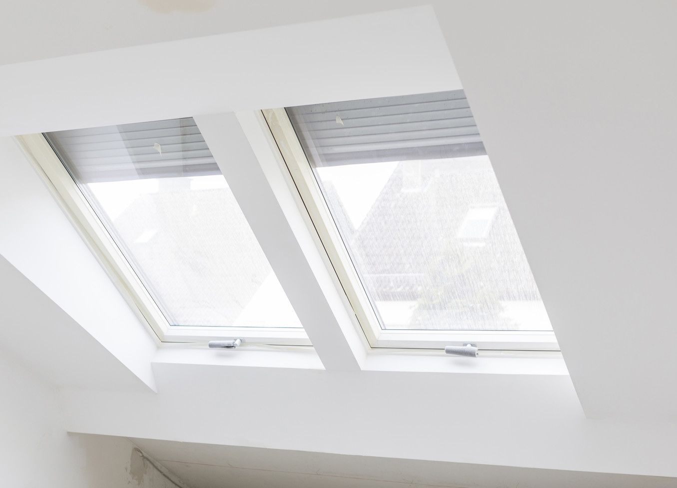 Deux fenêtres de toit blanches avec stores gris fermés.