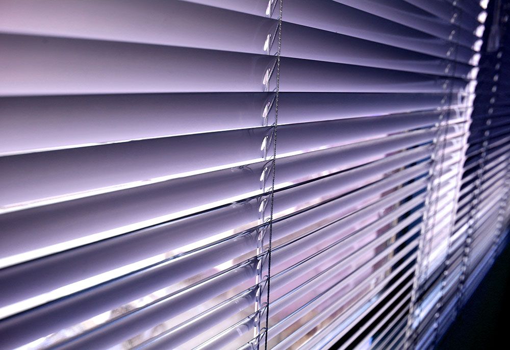 Vue rapprochée de stores de fenêtre violet clair, inclinés pour bloquer partiellement la lumière.