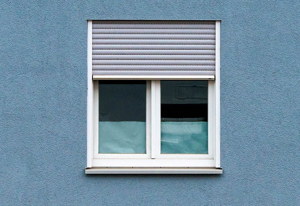 Fenêtre avec un volet roulant gris contre un mur bleu texturé.