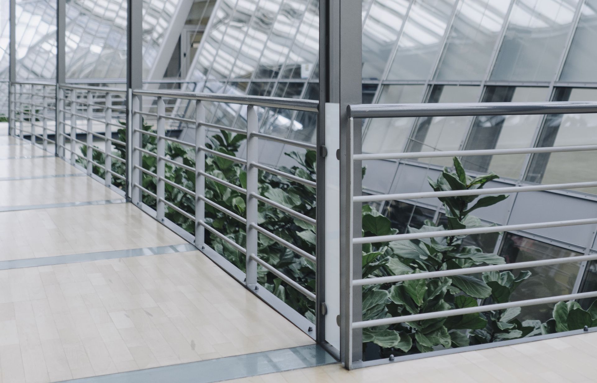Garde-corps en métal le long d'un couloir dans un immeuble moderne avec de grandes baies vitrées et des plantes.