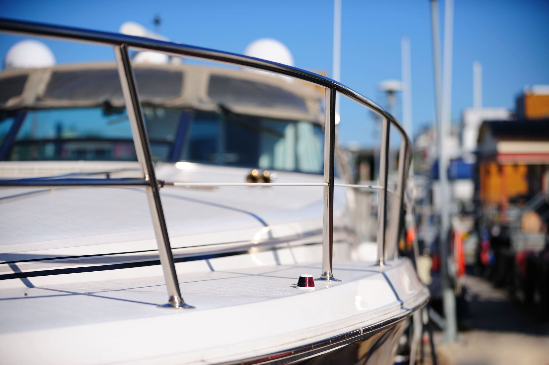 Yacht blanc avec rambarde en acier inoxydable, amarré dans une marina. Ciel bleu en arrière-plan.