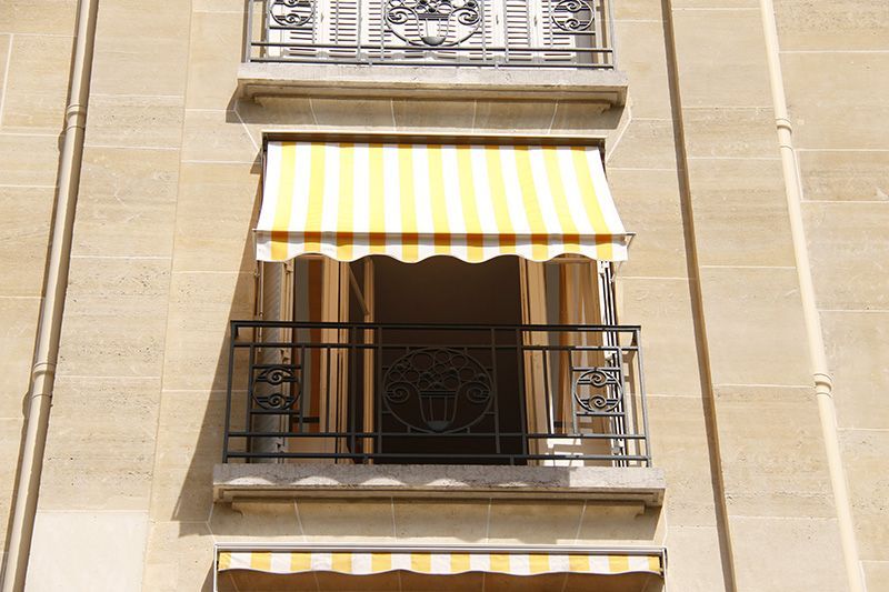 Auvent rayé jaune et blanc sur un balcon avec balustrade noire sur un bâtiment beige.