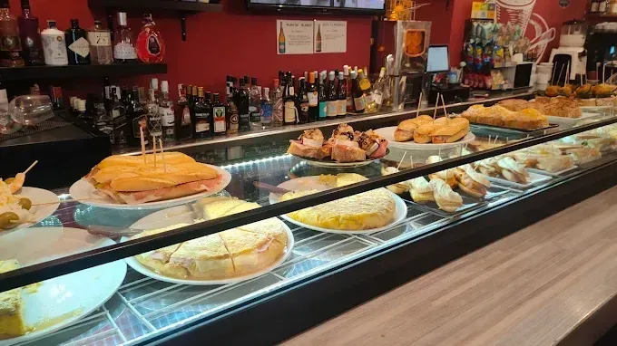 Vitrina repleta de tapas; una barra al fondo tiene botellas de licor y paredes rojas.