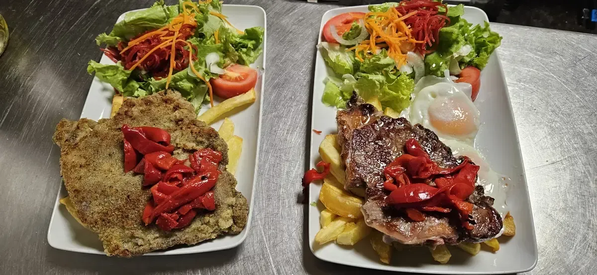 Interior de restaurante con mesas y sillas de madera, paredes de piedra y suelo de baldosas.