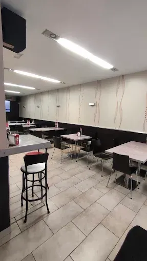 Interior de restaurante con mesas, sillas y barra. Paredes en tonos crema y marrón oscuro, suelo de baldosas e iluminación cenital.