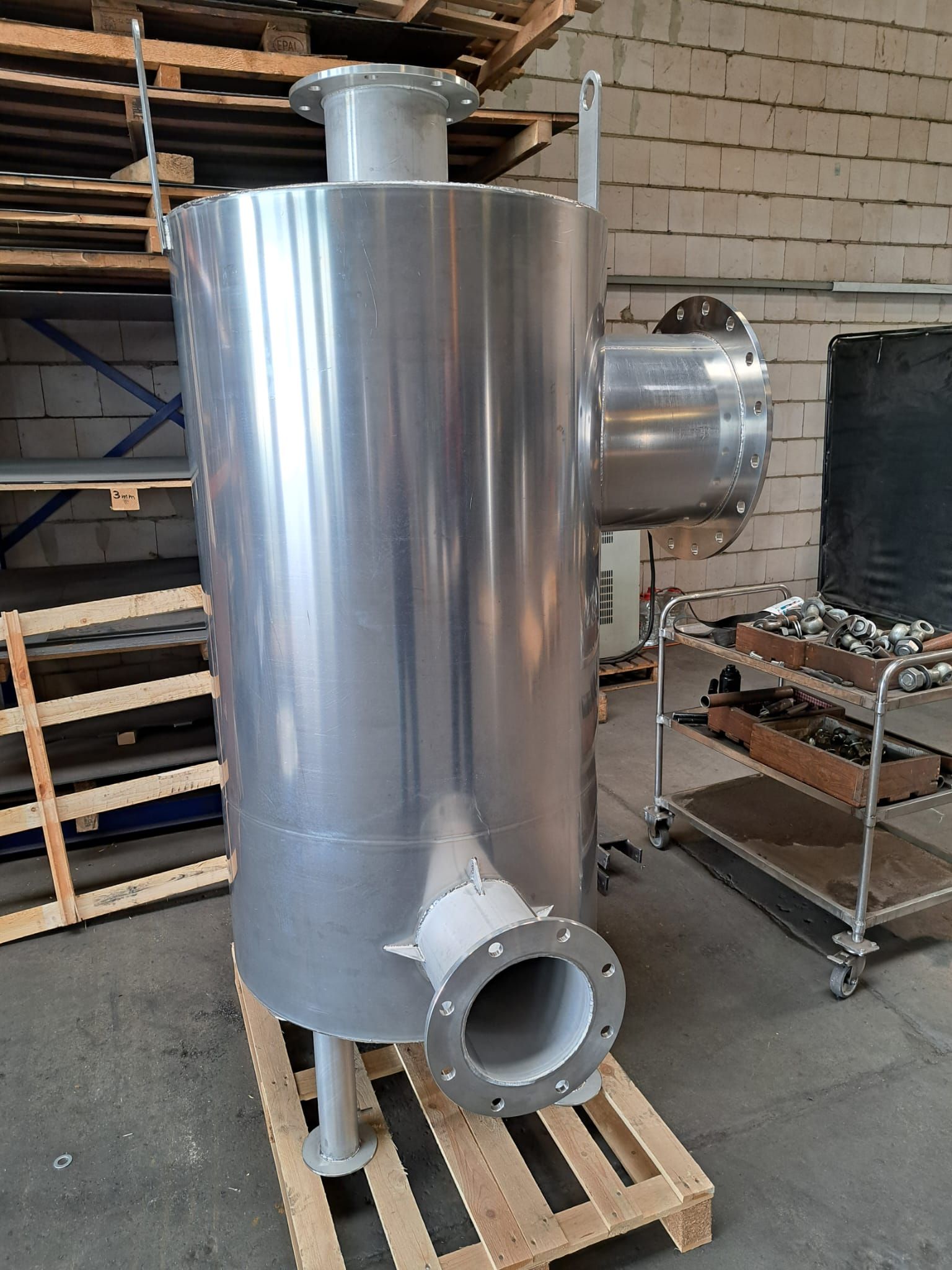 Ein großes Edelstahlrohr liegt auf einer Holzpalette in einem Lagerhaus.