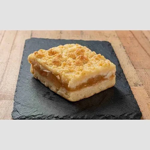 Un trozo de pastel de manzana reposa en un plato negro sobre una mesa de madera.