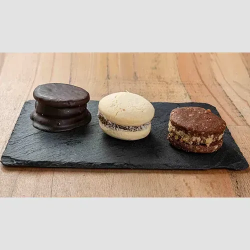Tres tipos diferentes de galletas están colocadas en una bandeja de pizarra sobre una mesa de madera.