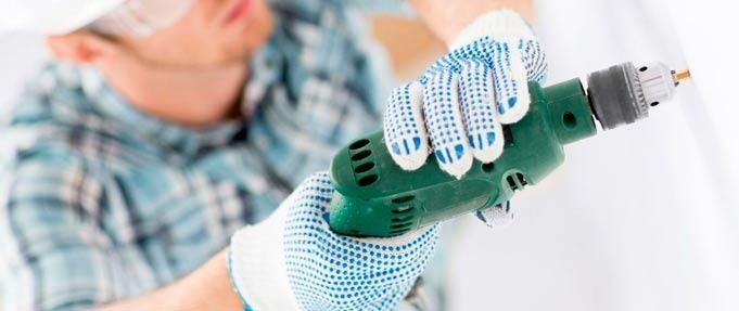 Un hombre que lleva guantes sostiene un taladro en su mano.