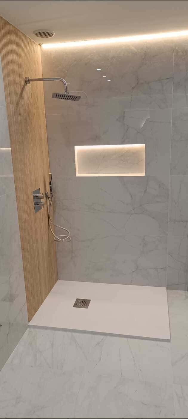 Ducha moderna con azulejos blancos, pared con acento de madera y desagüe de ducha rectangular.