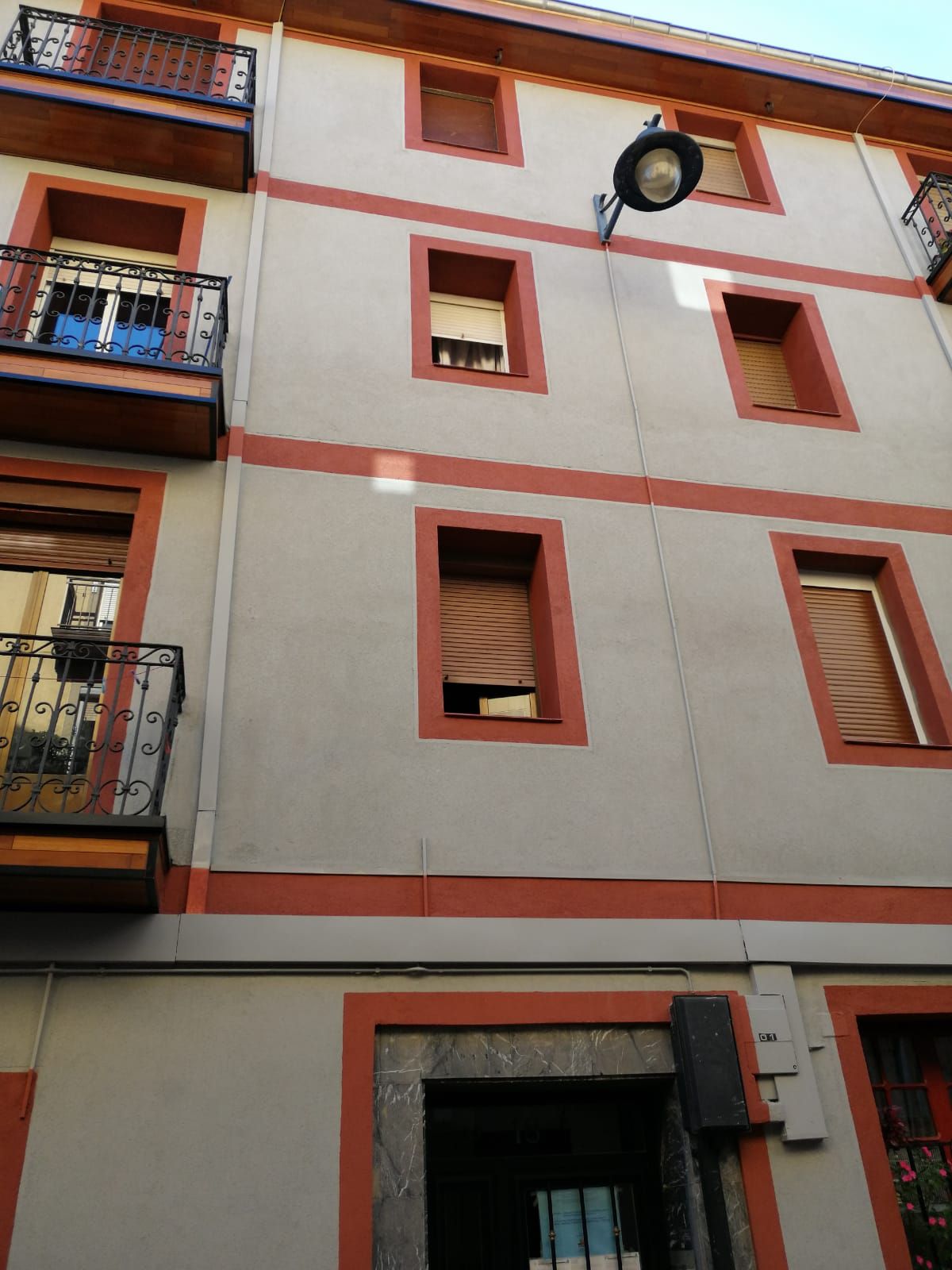 Edificio de varios pisos con fachada gris, molduras rojas, balcones y ventanas con contraventanas.