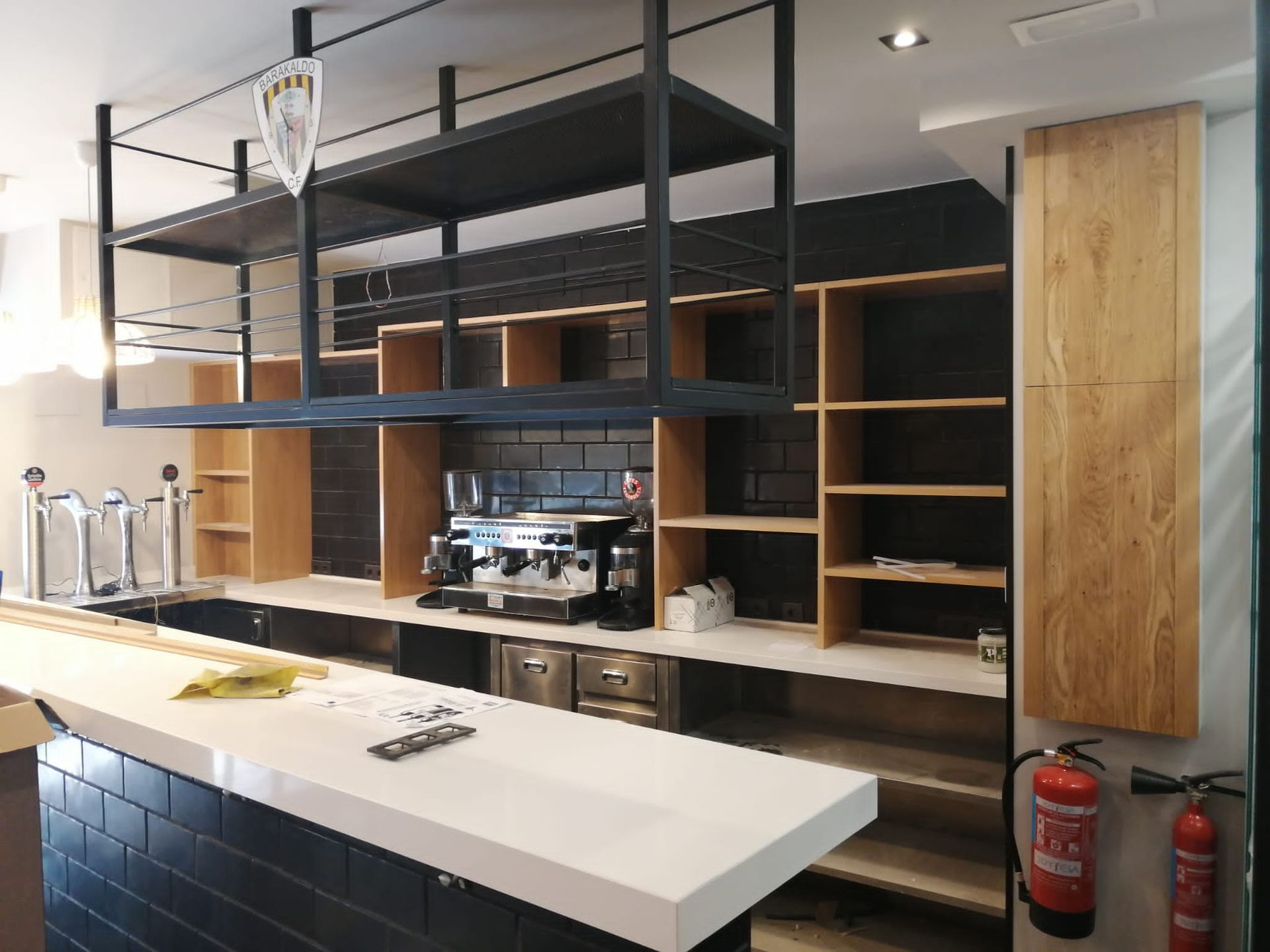 Interior de un bar en construcción con estanterías negras, detalles de madera y encimera blanca.