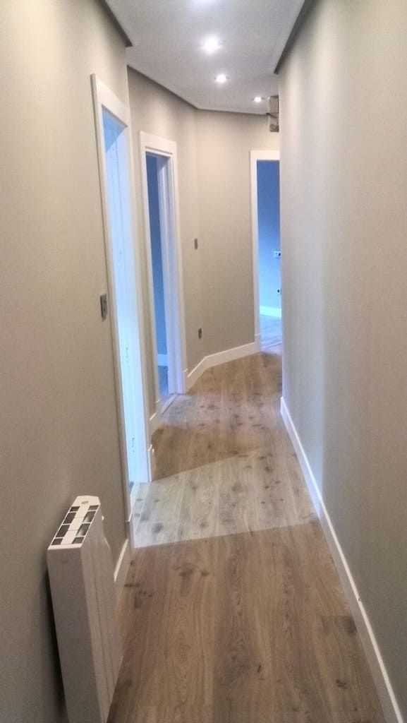 Pasillo estrecho con suelo de madera clara, paredes grises y marcos de puertas blancos. Hay un radiador a la izquierda.