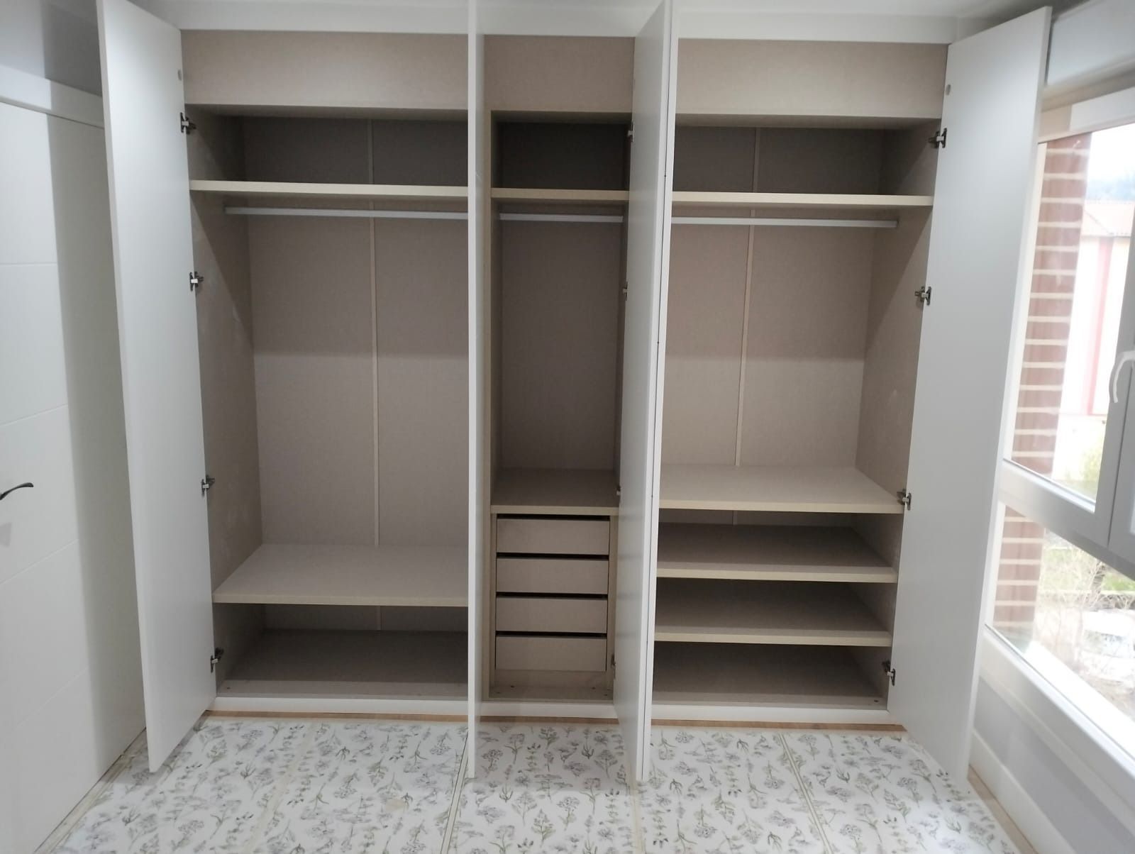 Armario blanco abierto con estantes, barras para colgar y cajones. Interior beige, puertas blancas.