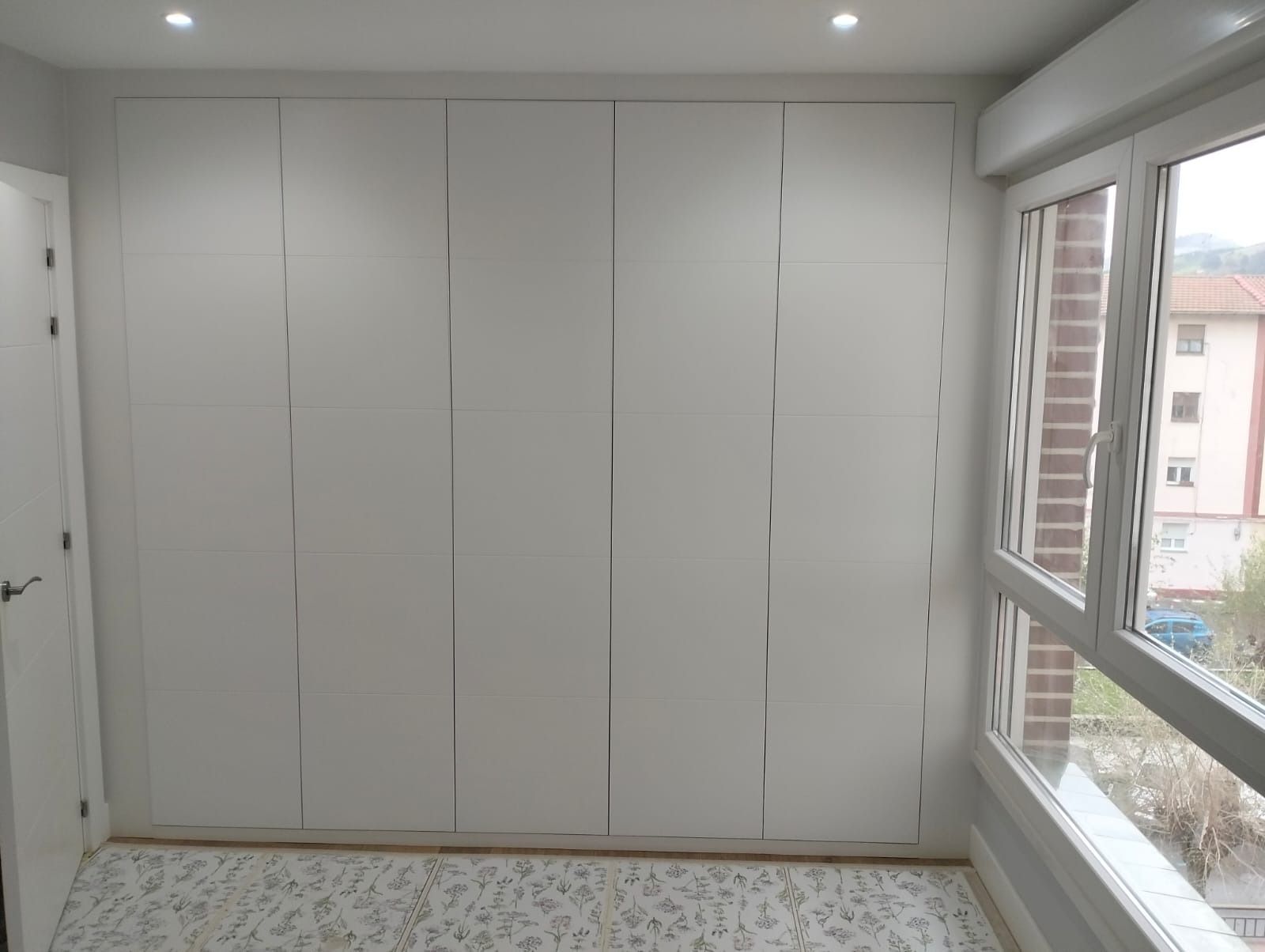 Puertas blancas de armario en una habitación con ventana a la derecha. Se ven las luces del techo.